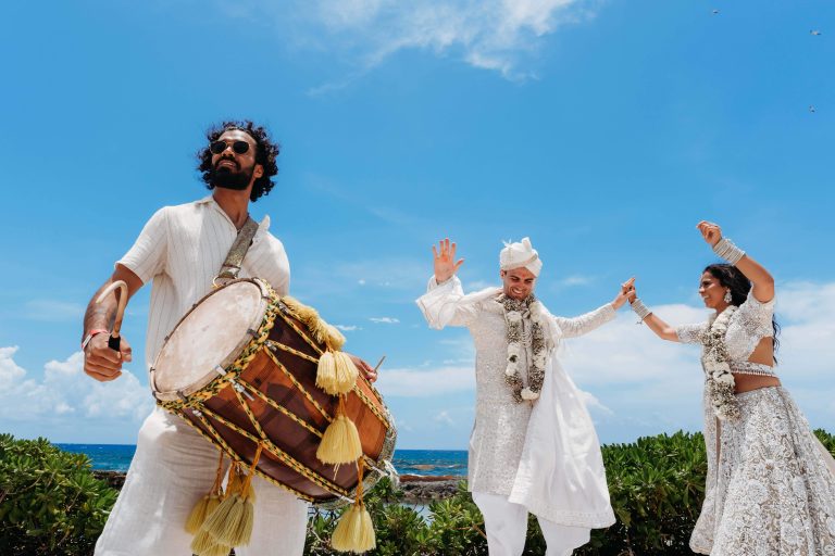 Beneath the luminous Cancun sky, radiant souls in white dance joyfully as vibrant drums echo, ocean waves blessing their union.